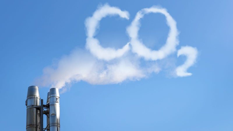 Der Rauch eines Industriekamins formt das Wort CO2 vor blauem Himmel
