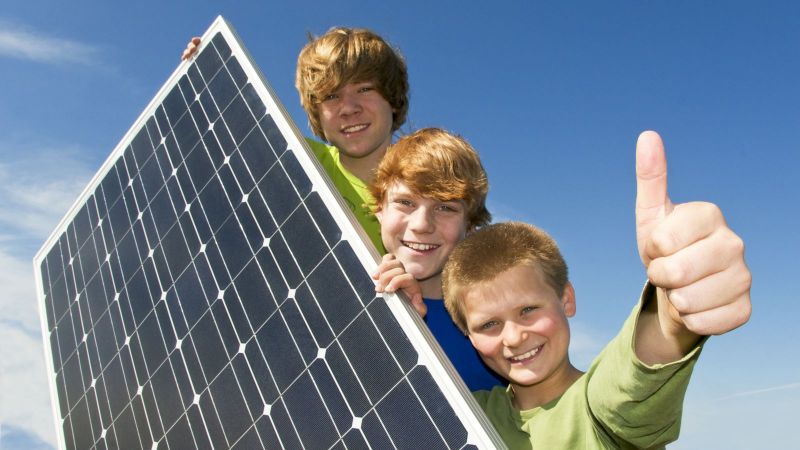 Drei Kinder stehen hinter einer Photovoltaikanlage.