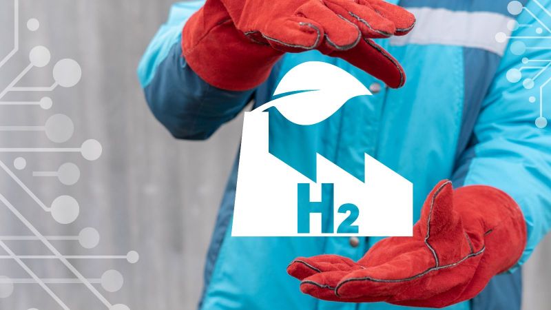 Eine person mit roten Handshcuhe hält ein Symbol einer Fabrik mit dem Schriftzug H2 zwischen seinen Händen.