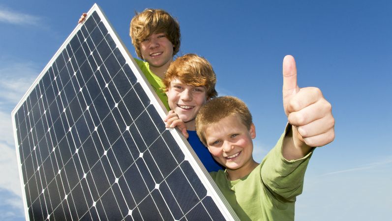 Drei Kinder, die hinter einer Photovoltaikanlage stehen.