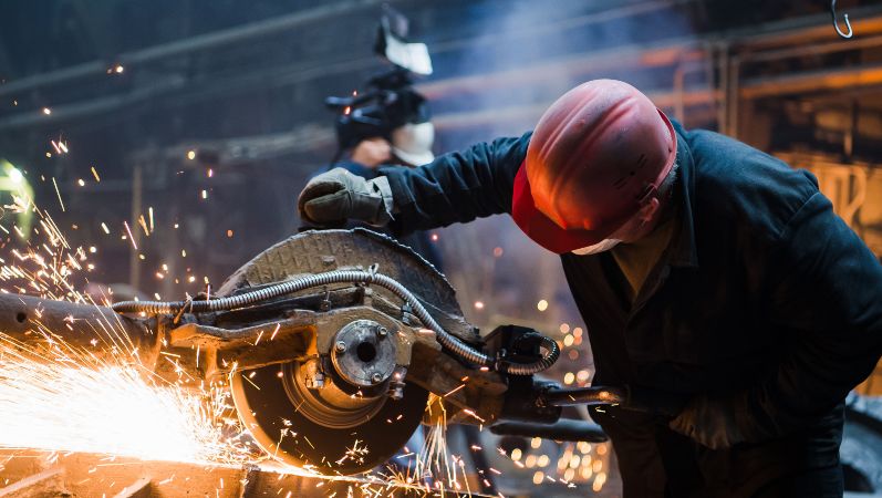 Ein Arbeiter schneidet heißes Metall mit einer Sägemaschine - es sprühen Funken.